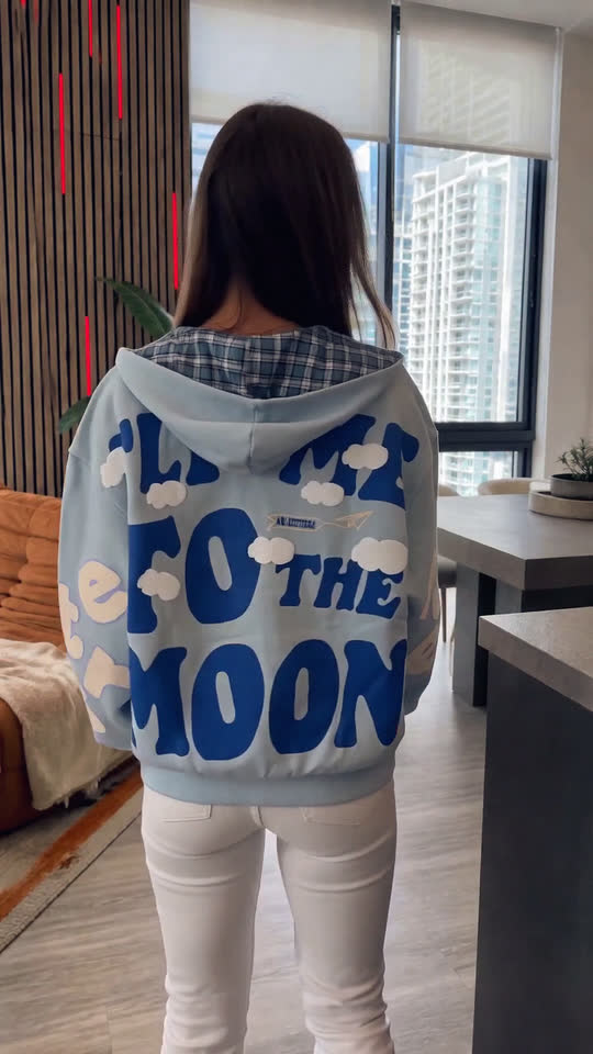 A woman layering a printed hooded sweatshirt over a cropped top in an apartment interior, showing how the layers sit together.